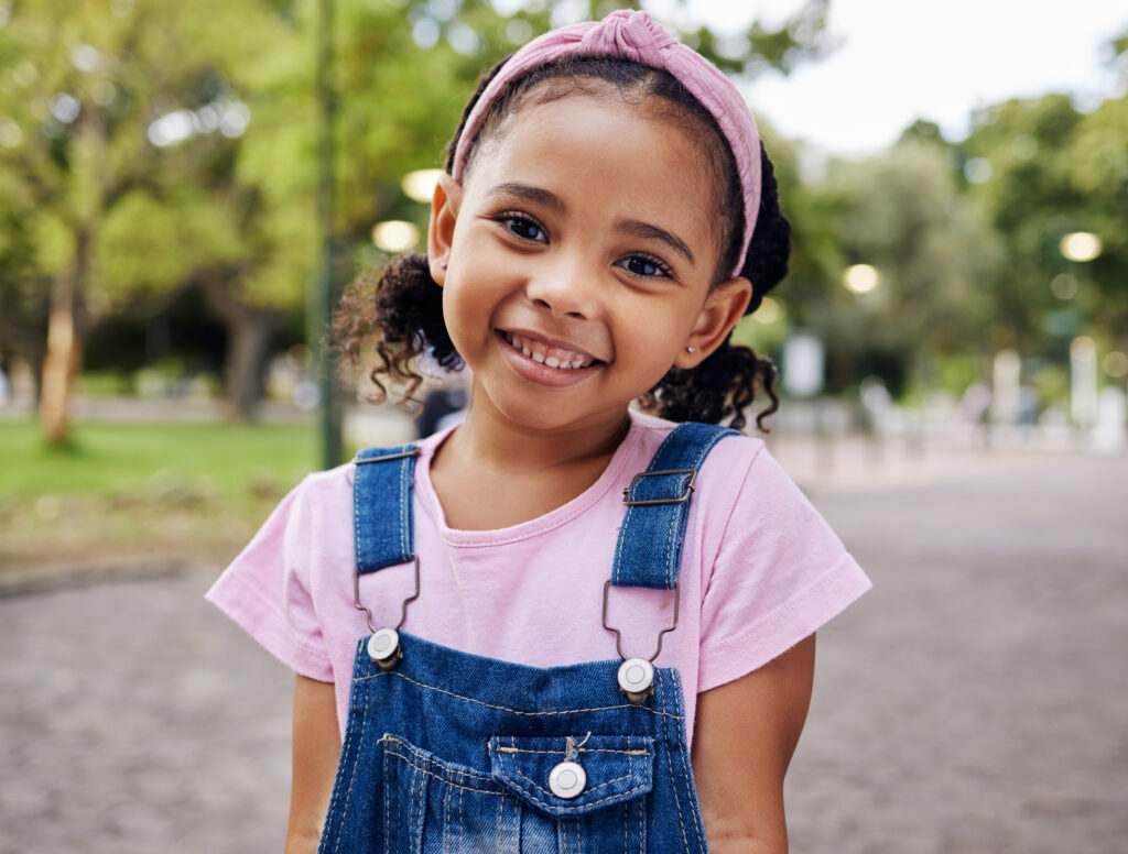 Young girl smiling in a park wearing overalls
