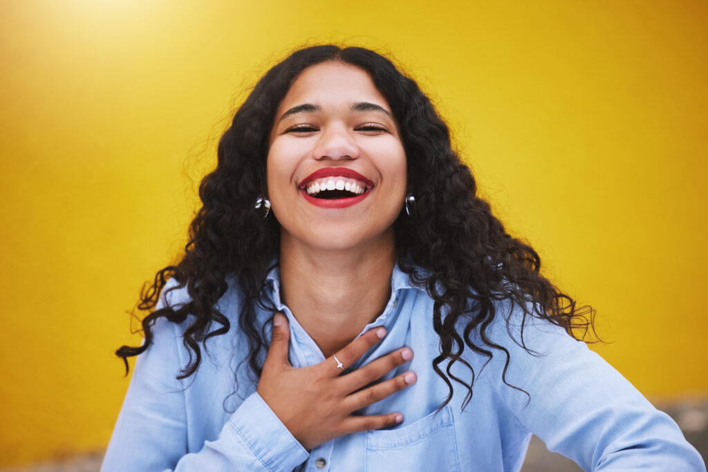 Happy, smile and fun with a woman laughing and joking in studio against a yellow background. Carefree, joy and humor with an attractive young female standing inside on a bright and colorful wall.