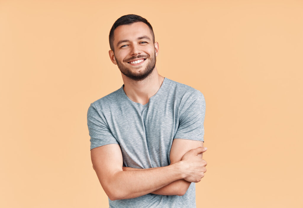 Happy smiling handsome man with crossed arms looking to camera over beige background.