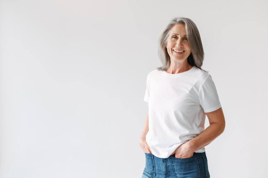 Grey senior woman in t-shirt smiling and looking at camera isolated over white background
