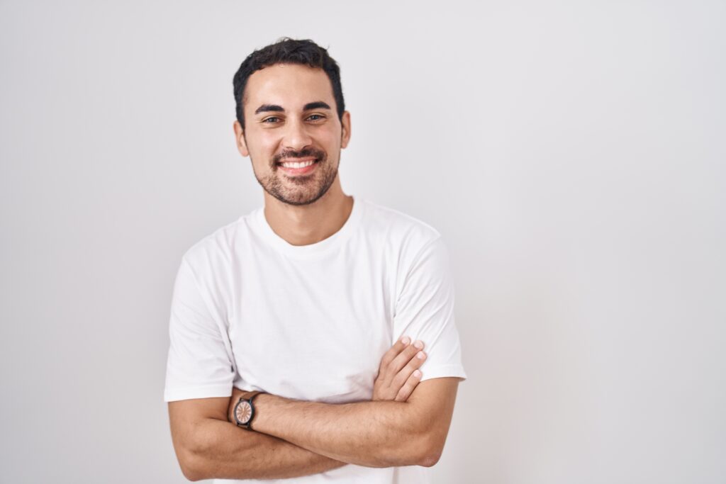 Handsome hispanic man standing over white background happy face smiling with crossed arms looking at the camera. positive person.